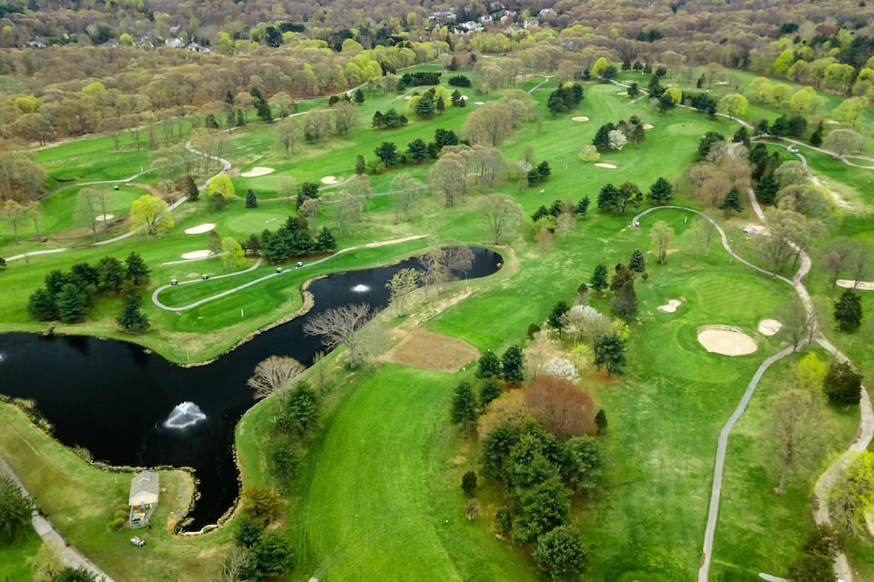 An aerial view of a golf course with a pond, sand bunkers, and a winding path.