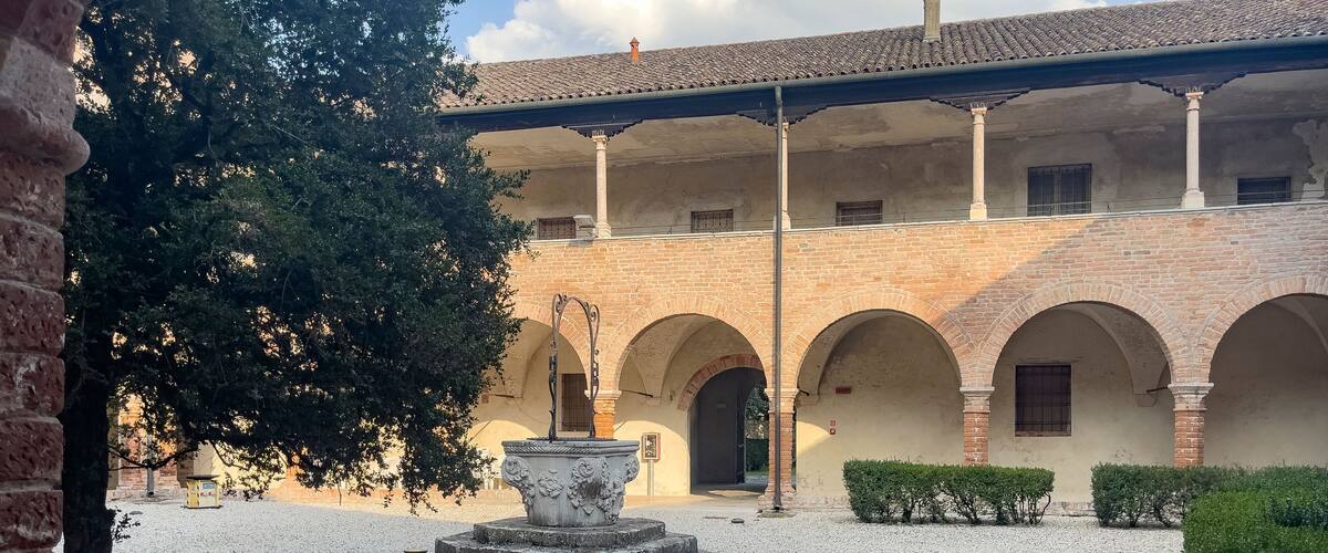A courtyard with a fountain, arches, and a building with a tiled roof.