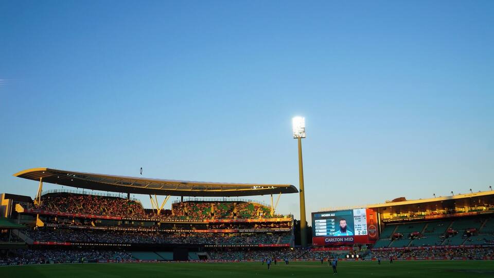 A stadium with a large crowd, a scoreboard, and a tall light pole.