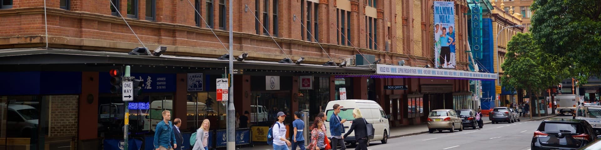 A street with pedestrians, cars, and a historic building with a theater.