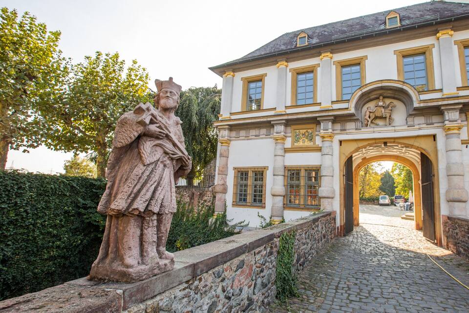 Ein historisches Gebäude mit einer Statue einer Person in historischen Gewändern, einem Rundbogenportal und einem Kopfsteinpflasterweg.
