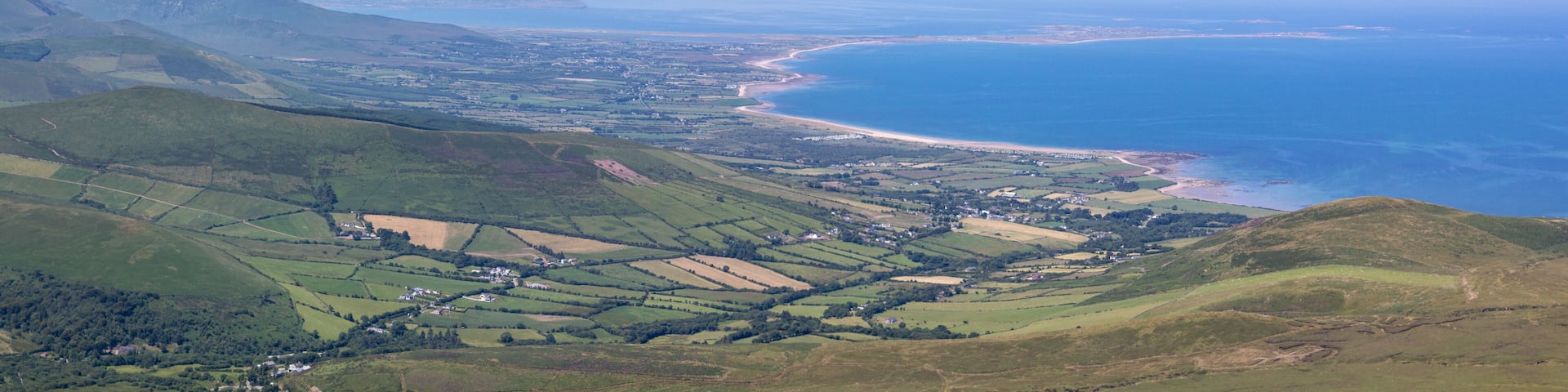 A coastal landscape with rolling hills, a beach, and a distant mountain range.