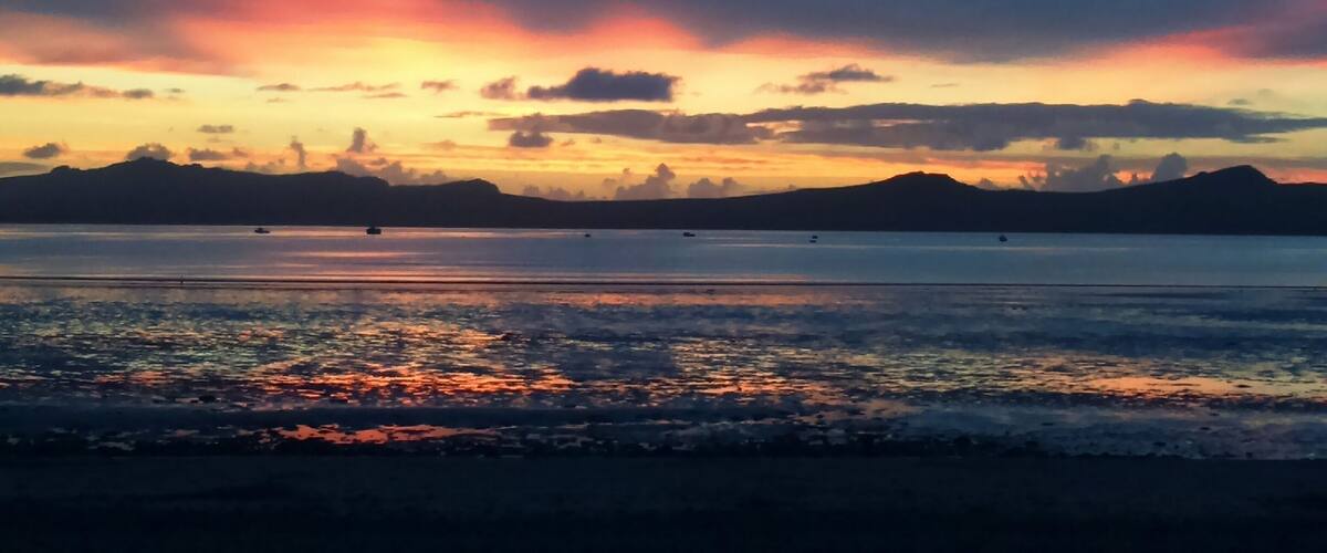 A sunset over a calm body of water with boats and distant mountains.