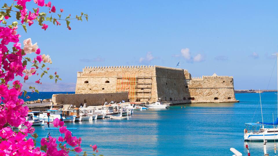 A historic stone fortress by a harbor with boats docked in the background.