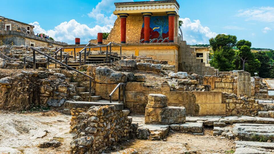 Ancient ruins with stone steps and columns, a mural, and a clear blue sky.
