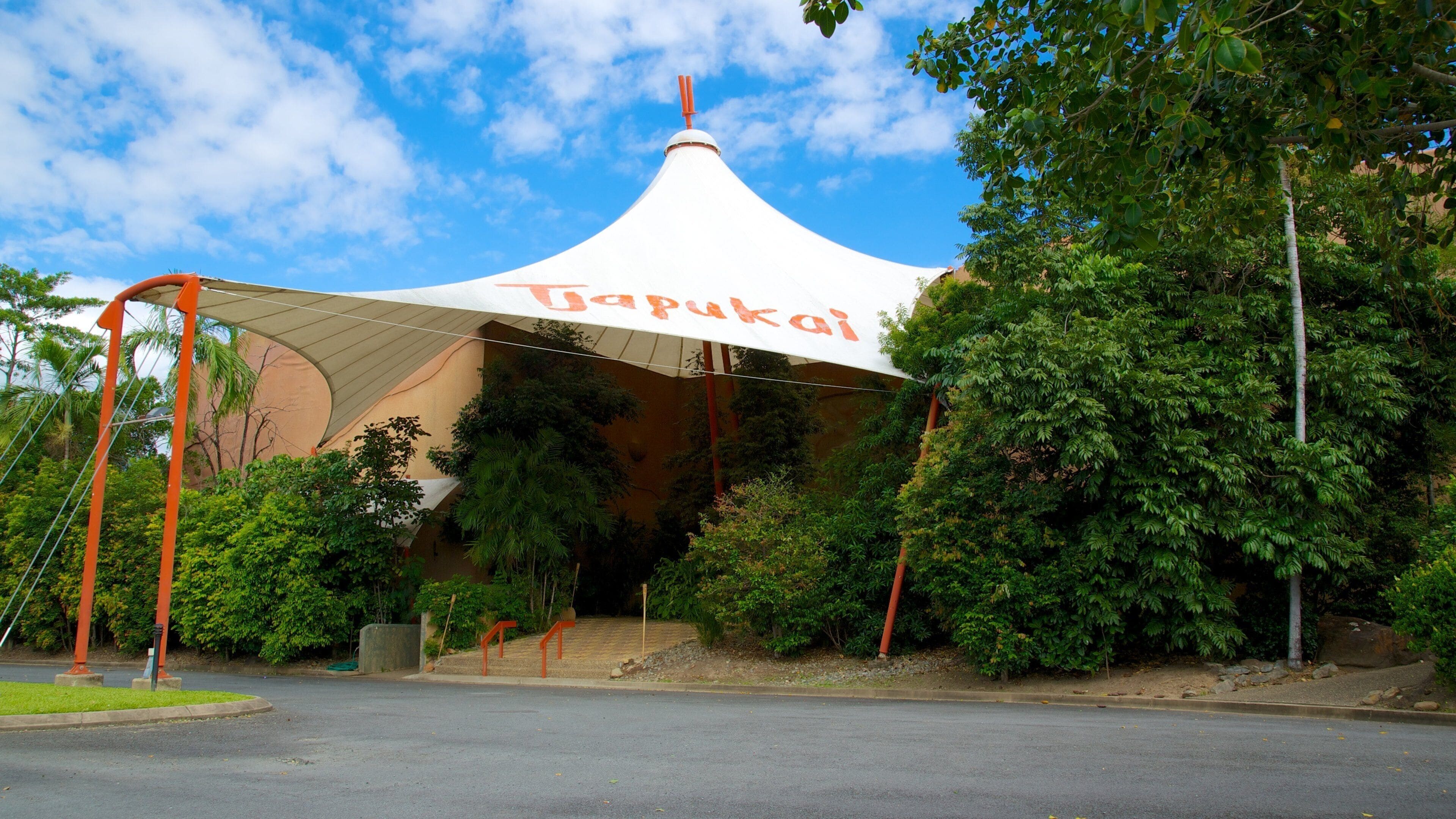 A white pavilion with 'Tapukai' written on it, surrounded by greenery and trees.