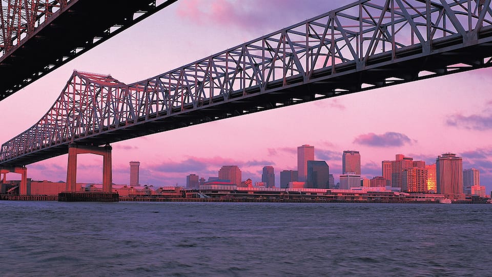 A bridge spanning a body of water with a city skyline in the background during sunset.
