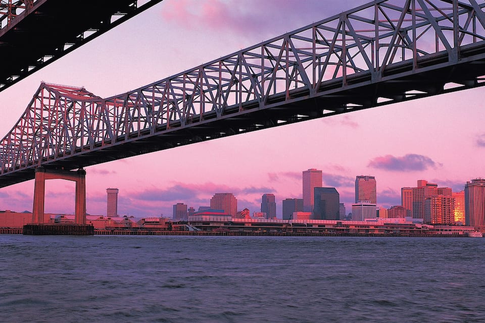 A bridge spanning a body of water with a city skyline in the background during sunset.