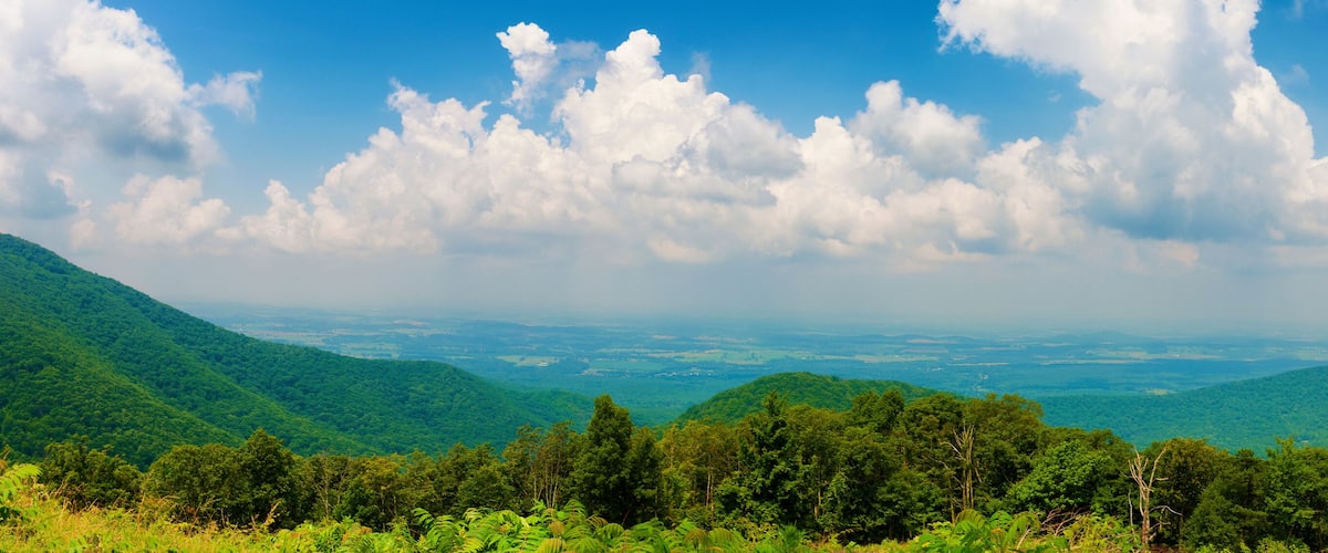 A lush green valley with rolling hills and a partly cloudy sky.