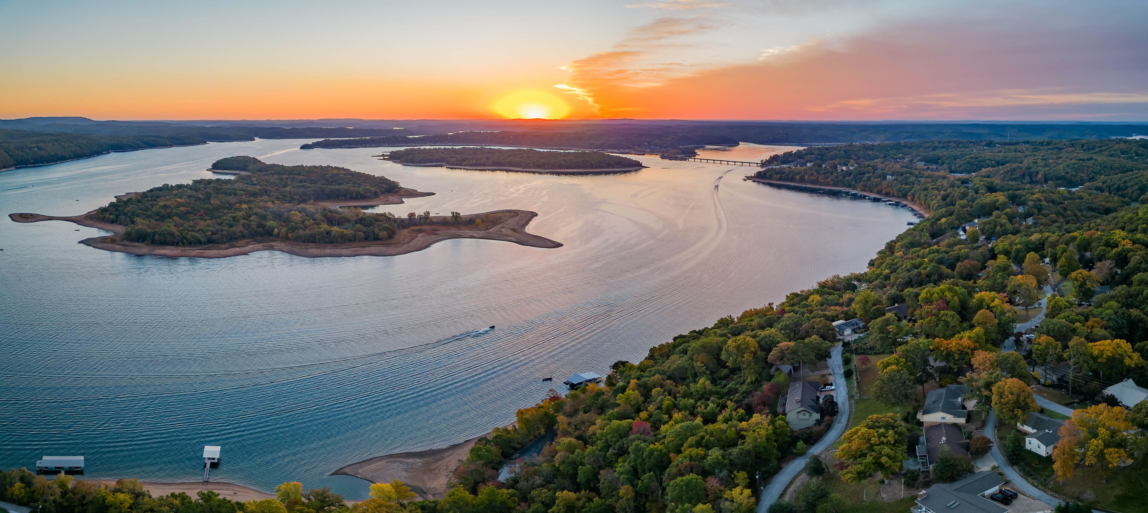 A river with multiple islands, a bridge, and a residential area with autumn foliage.