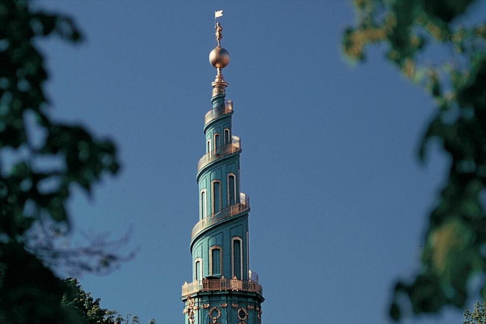 A tall tower with a spire and a flag at the top, surrounded by trees.