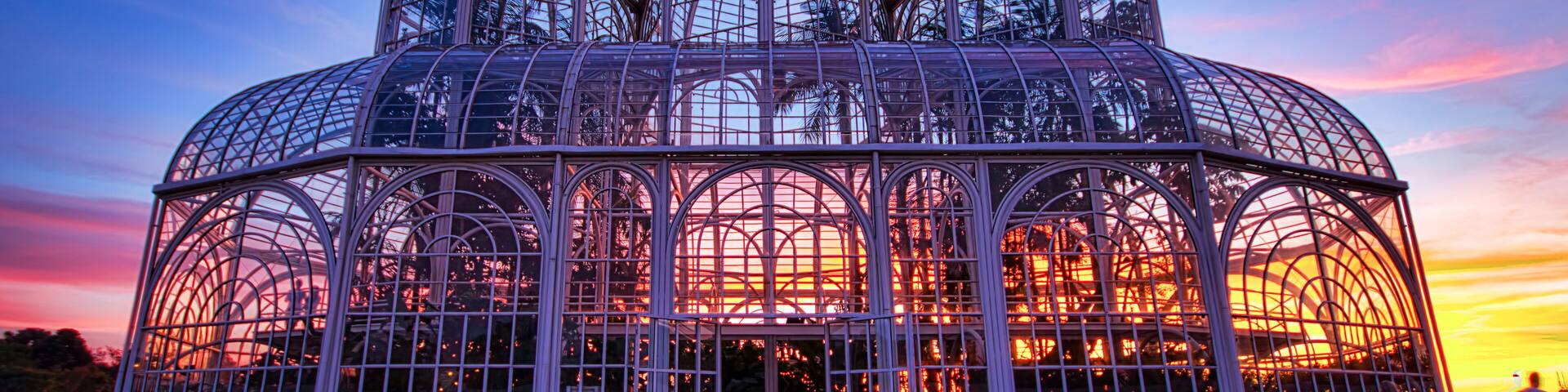 A large glass greenhouse structure with multiple domes, surrounded by a grassy area.