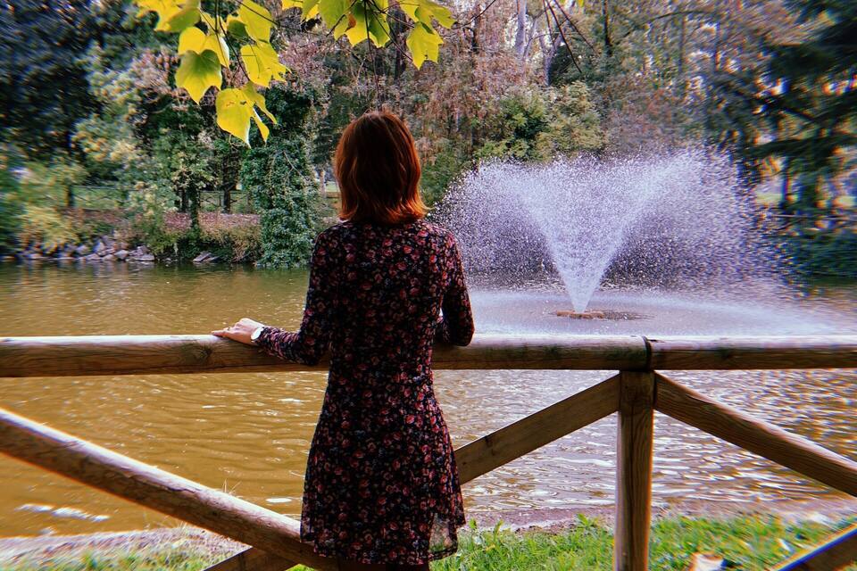 Une femme se tient près d’une clôture en bois, d’où elle peut admirer un étang agrémenté de jets d’eau.