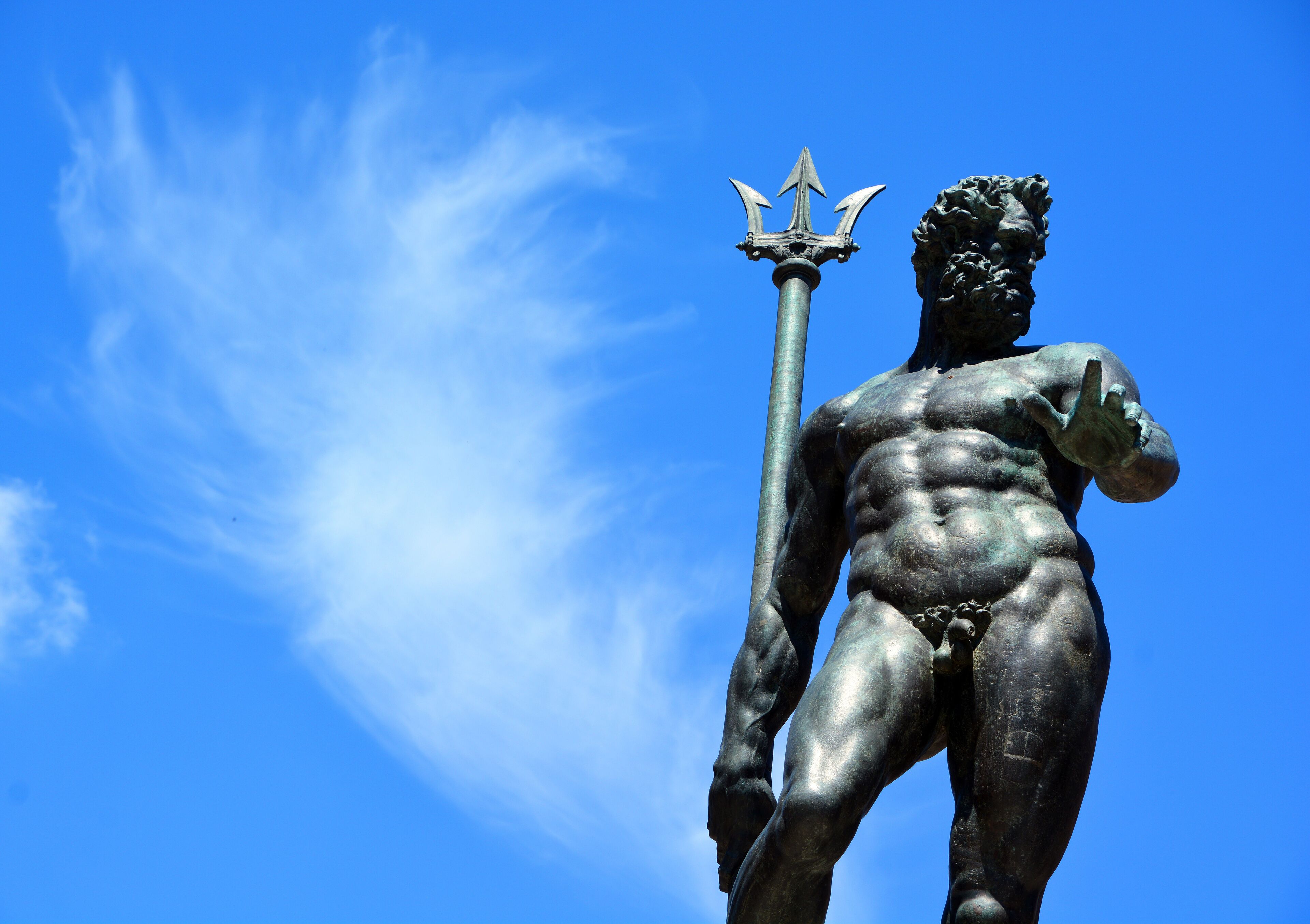 Una estatua de bronce de una figura musculosa sosteniendo un tridente, con un cielo azul despejado de fondo.