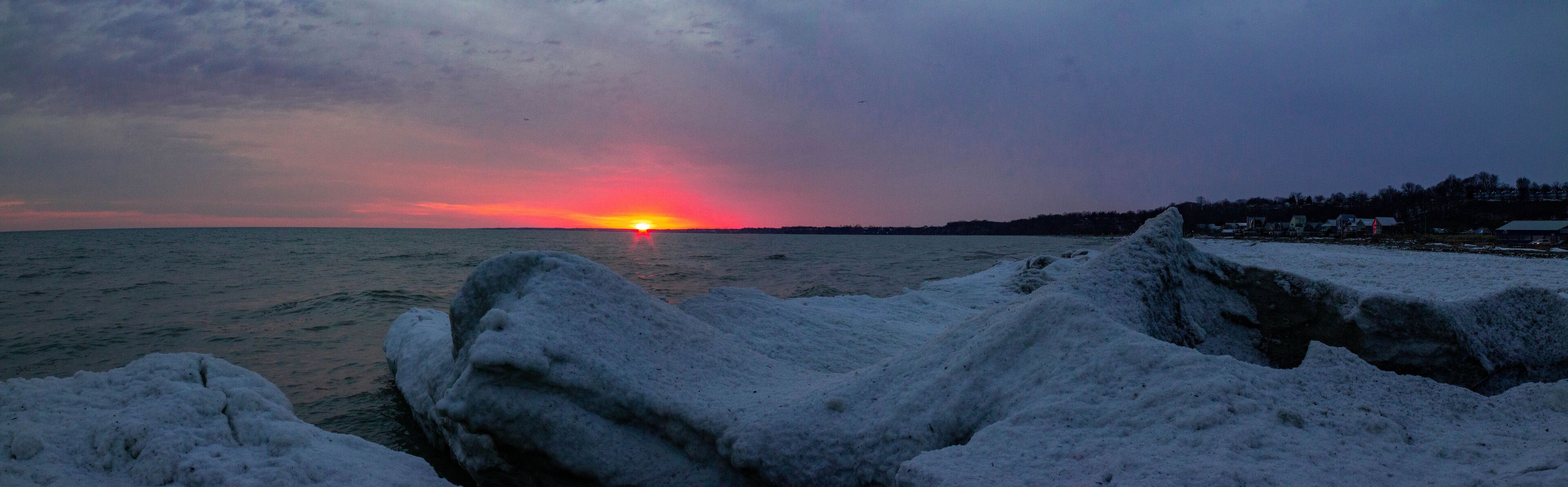 Pôr do sol sobre uma paisagem nevada com formações de gelo em primeiro plano.