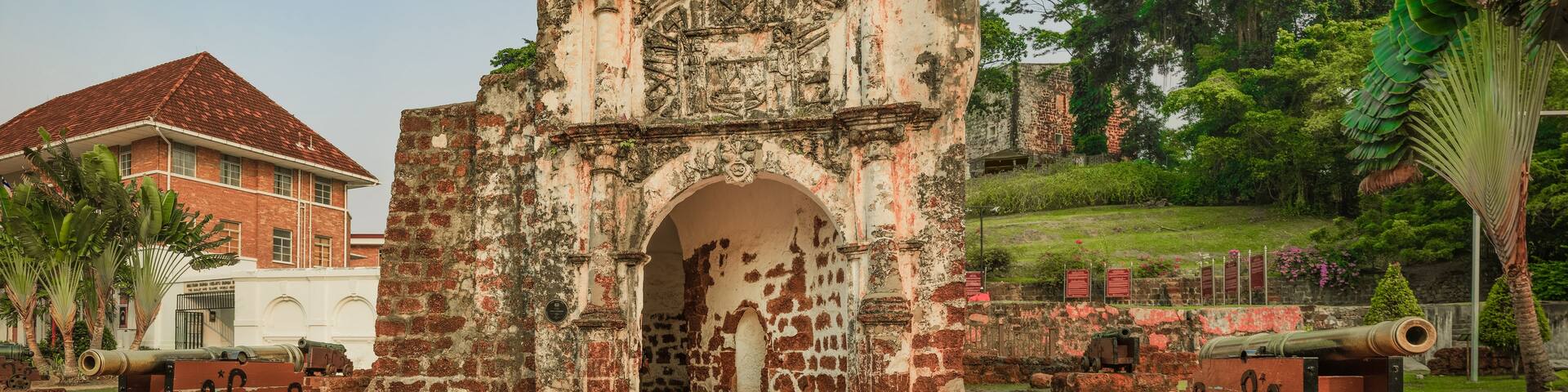 An ancient stone structure with a central archway, surrounded by brick walls and two cannons.