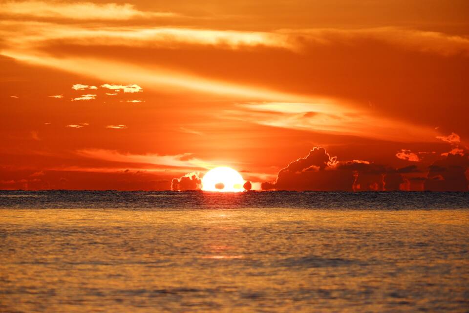 A sunset over the ocean with the sun partially obscured by clouds.