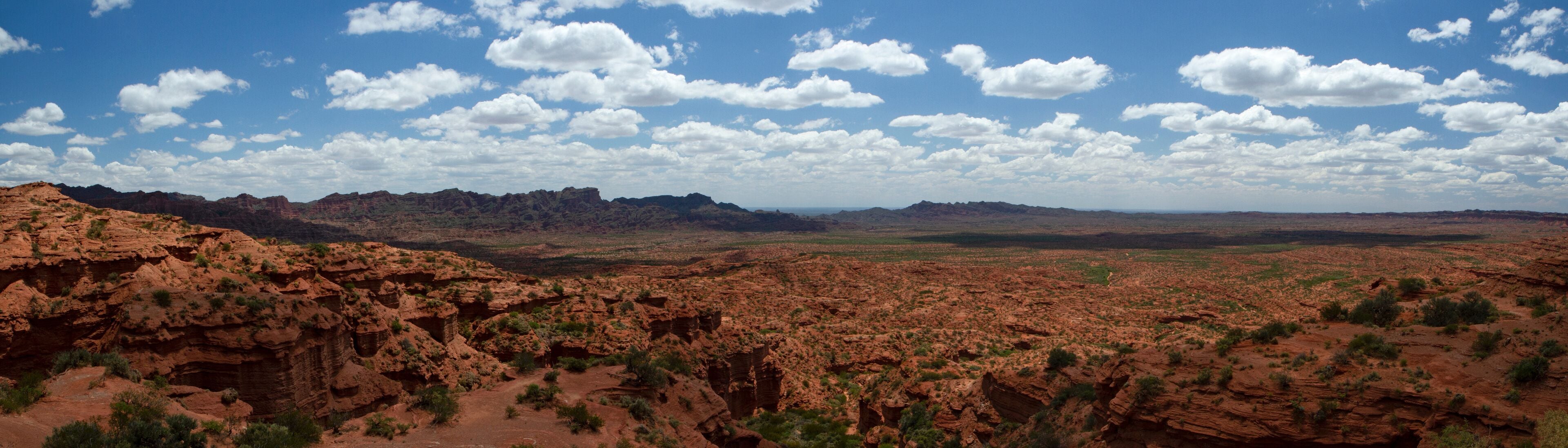 The red canyon. Panorama view of the arid desert, sandstone and rocky cliffs and mountains under a blue sky with clouds.