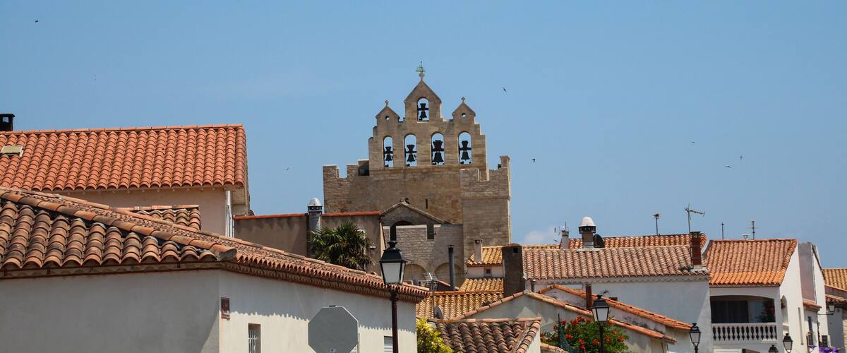 A historic building with a bell tower, surrounded by white buildings with red-tiled roofs.