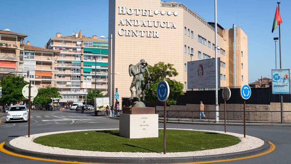 A roundabout with a statue, Hotel Andalucía Center, and a flag.