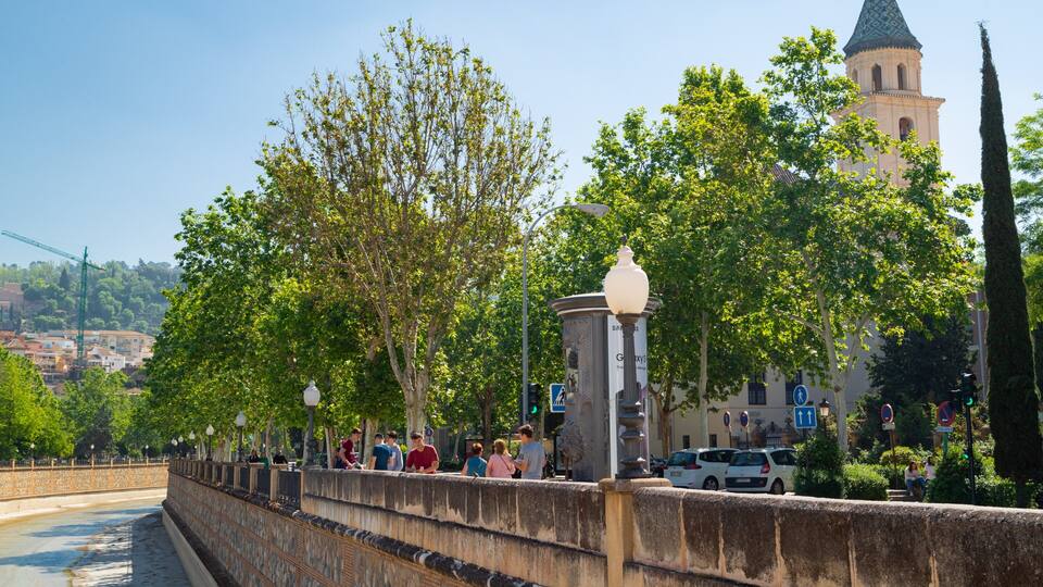 A bridge with a stone railing, trees, and a tower in the background.