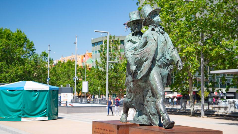 A bronze statue of a man with a hat and cane in a public square.