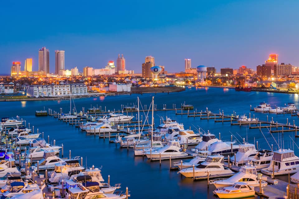 Un port de plaisance où sont amarrés de nombreux bateaux, avec la silhouette d’une ville en arrière-plan et un ciel dégagé.