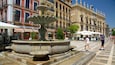 A historic plaza with a central fountain, surrounded by colorful buildings and outdoor seating areas.