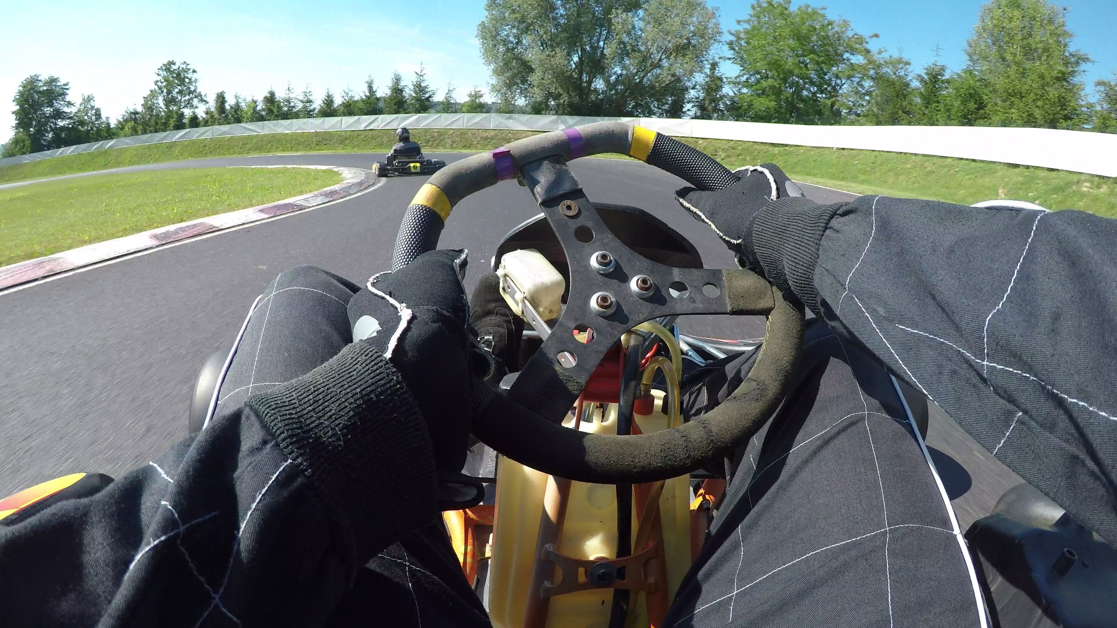 POV: Steering a speeding go cart along the winding asphalt circuit on sunny day.