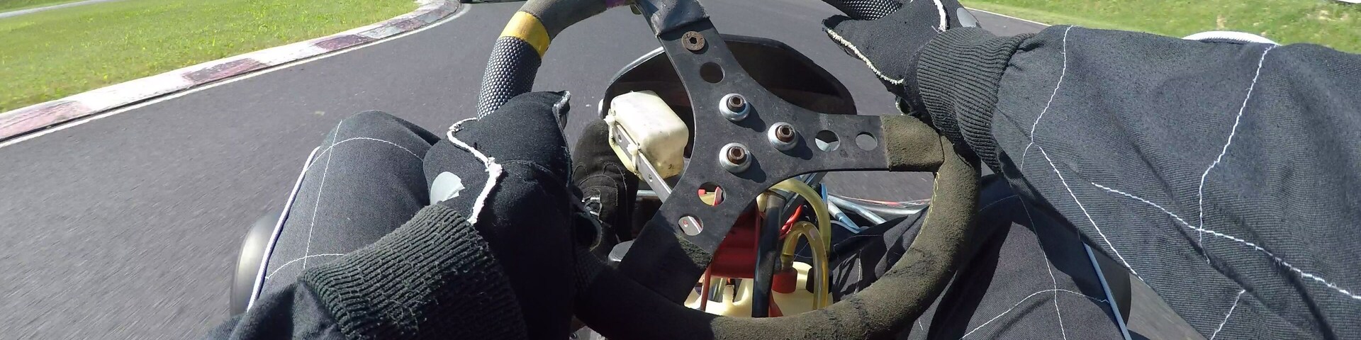 POV: Steering a speeding go cart along the winding asphalt circuit on sunny day.