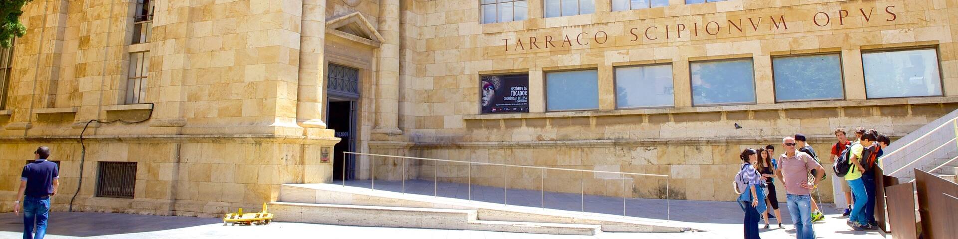 A historic building with classical architecture and a sign reading "TARACO SCIPIONVM OPVS".