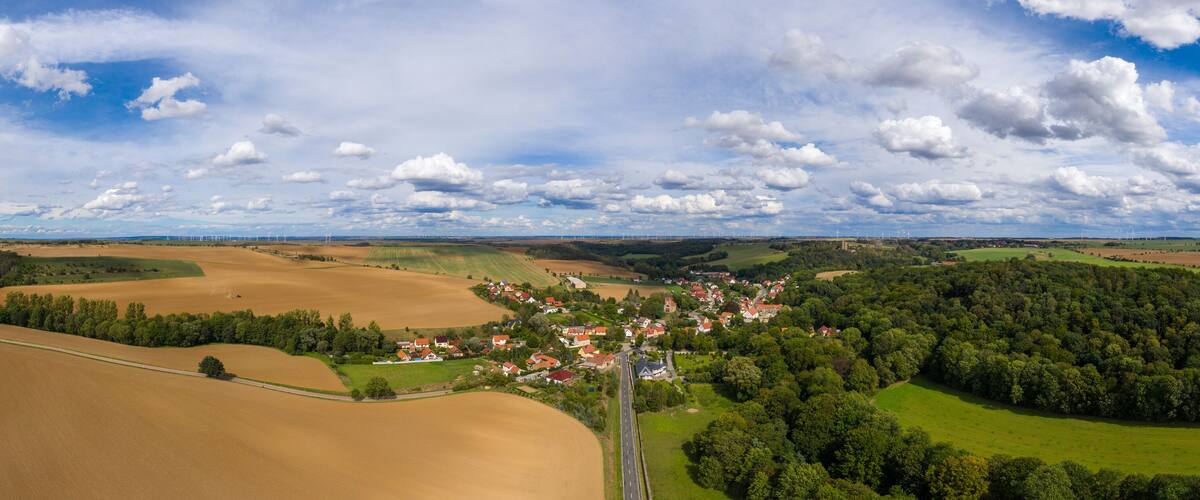 A rural landscape with a village, fields, and wind turbines.