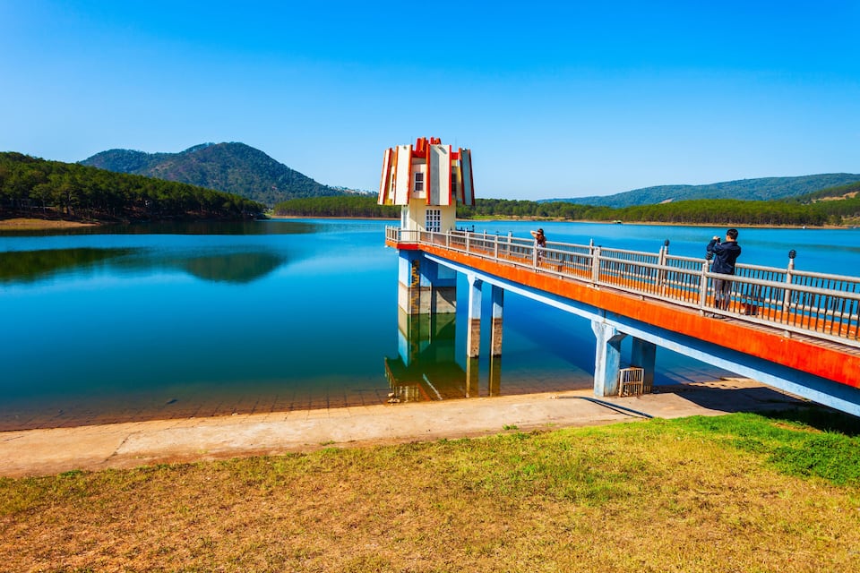 A bridge over a calm lake with a small tower, surrounded by hills.