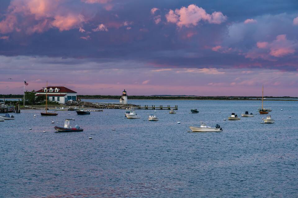 A harbor with multiple boats, a lighthouse, and a building with a red roof.