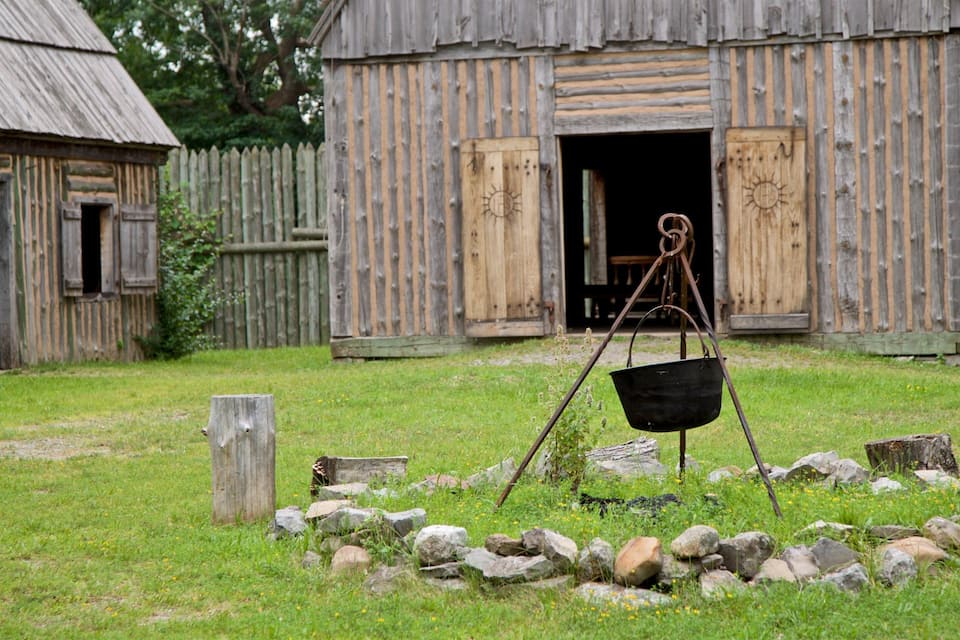 A rustic wooden barn with a metal bucket on a stand in front.