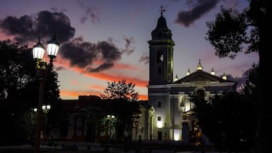 A church with a tall bell tower and a dome, surrounded by trees and street lamps.