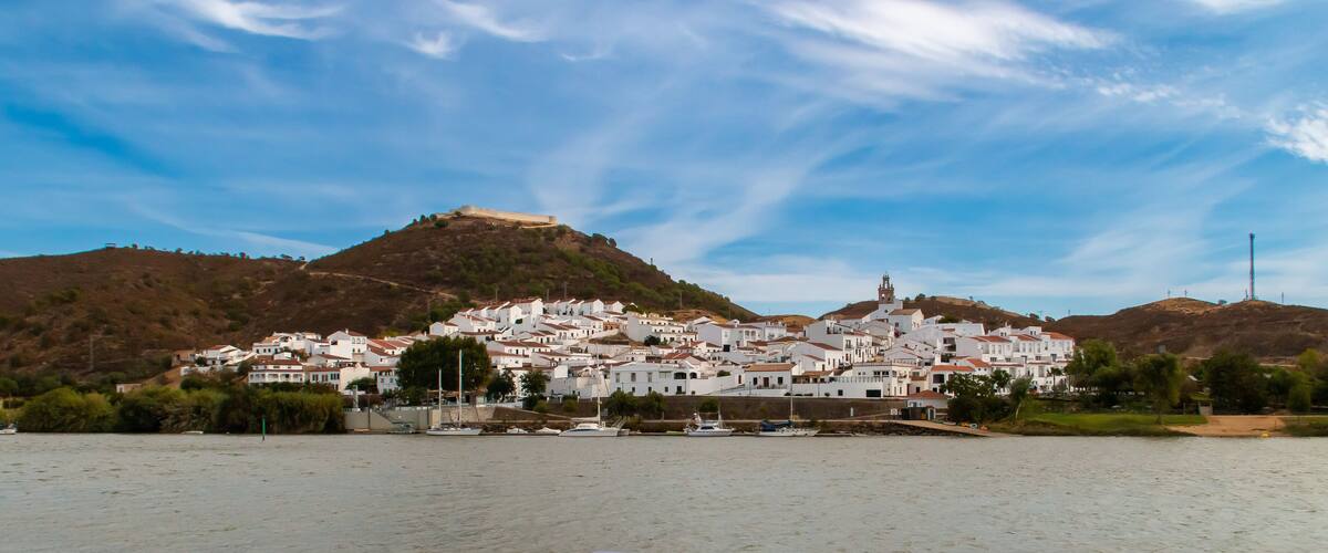 A coastal town with white buildings, a hilltop church, and boats in the foreground.