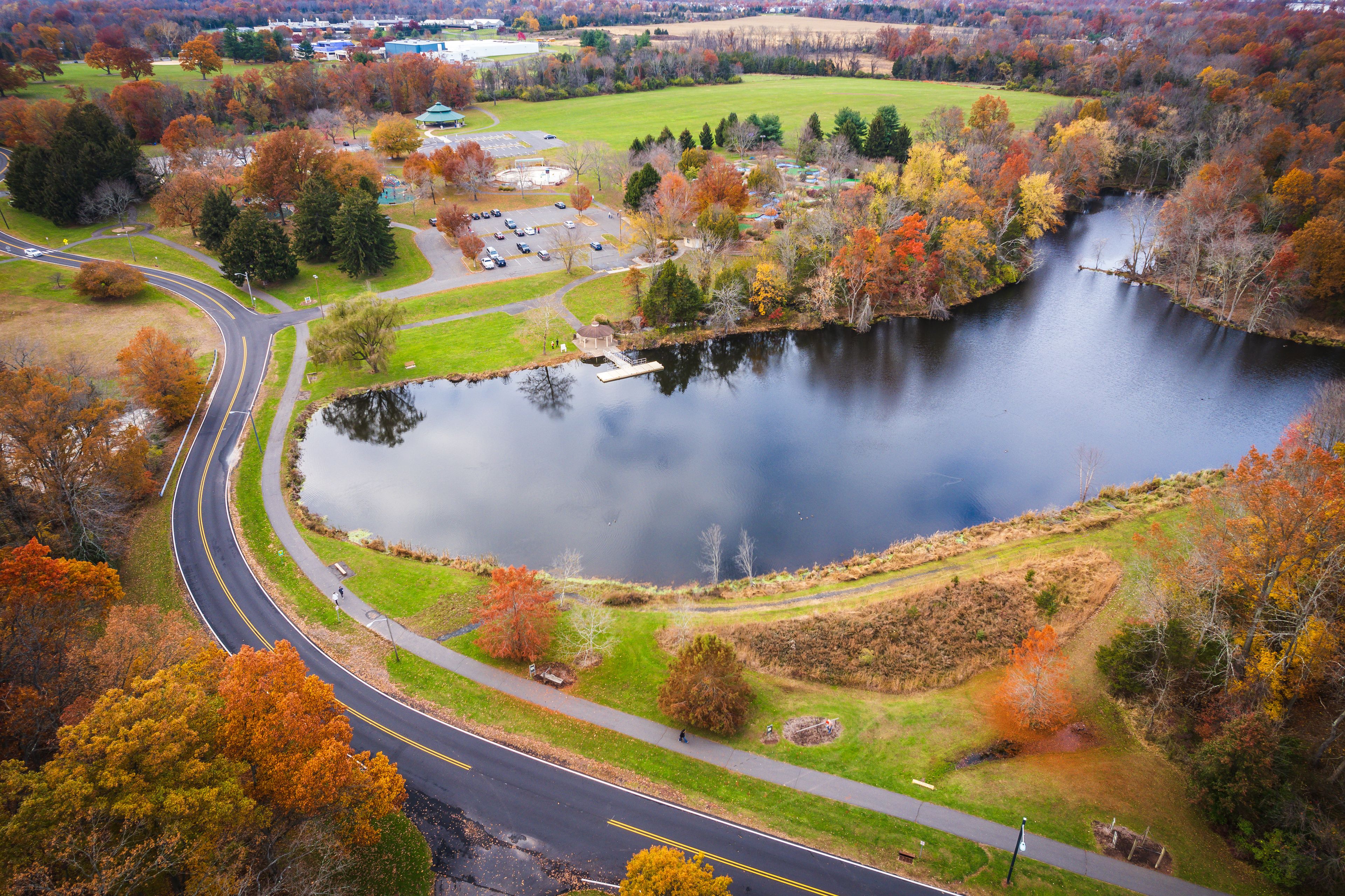 A lake surrounded by autumn foliage, a winding road, and a small gazebo.