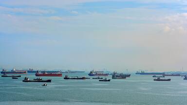 A harbor with multiple cargo ships and a small boat in the foreground.