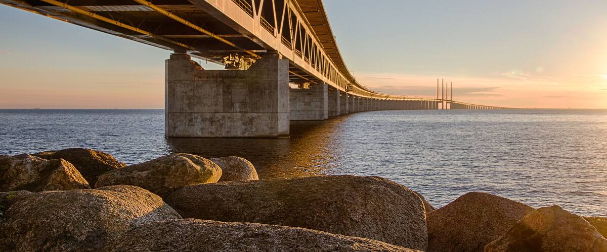 A bridge over water with large rocks in the foreground.