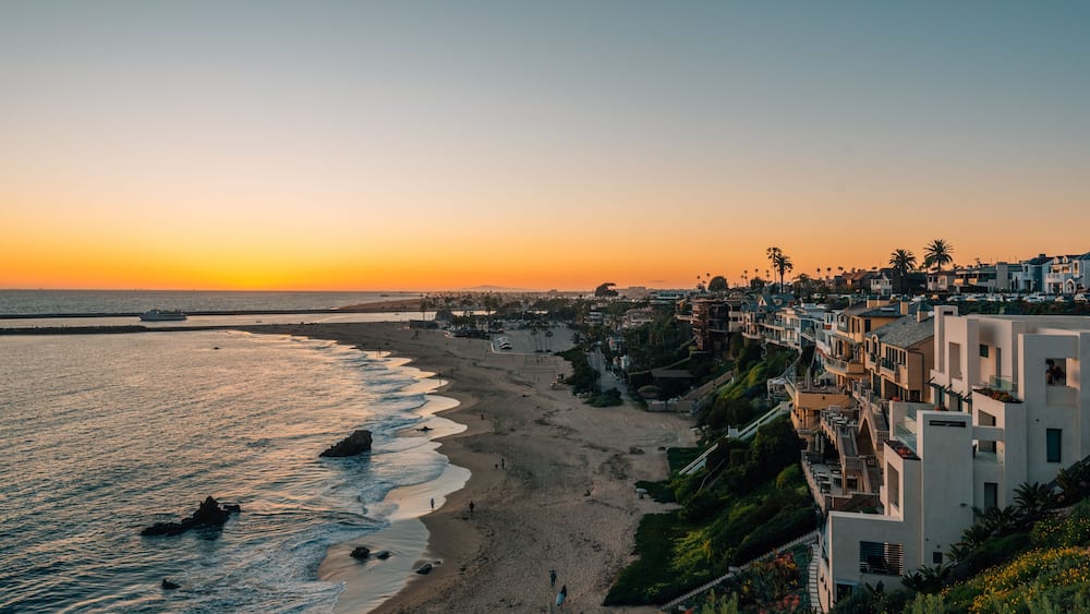 A coastal cityscape with a beach, ocean, and residential buildings during sunset.