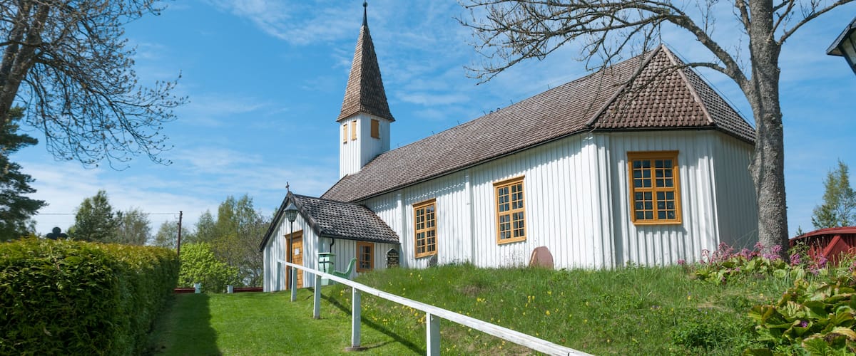 A white church with a tall steeple and a red roof, surrounded by green grass and trees.