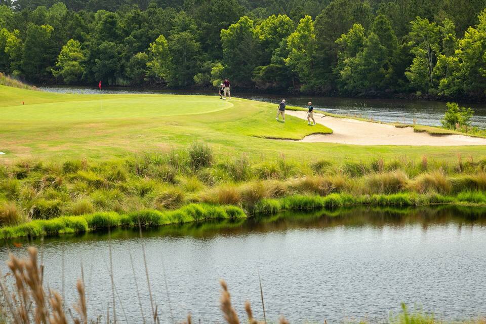 A golf course with a pond, sand bunkers, and a forested area.