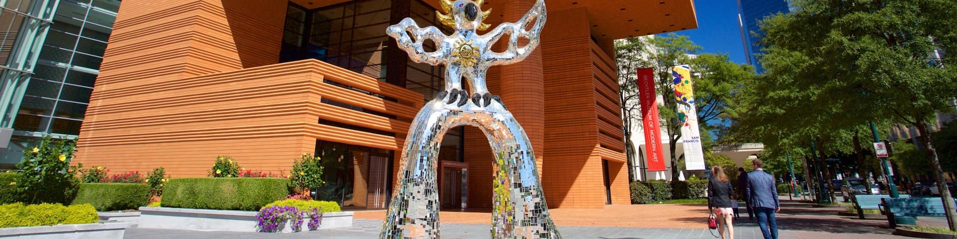 A modern building with a distinctive arched entrance and a mosaic sculpture in front.