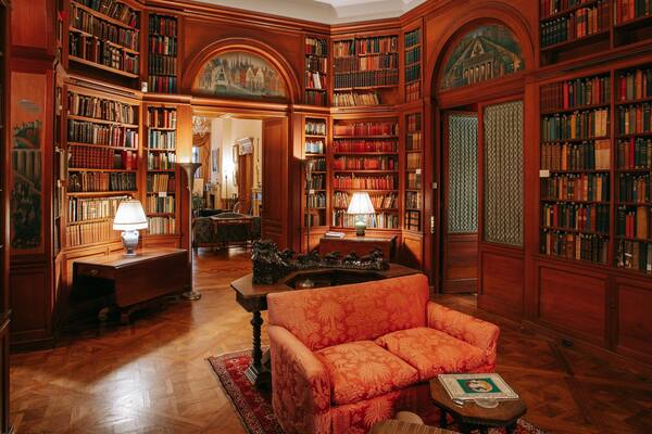 Eine Bibliothek mit Holzbögen, einem roten Sessel und einem Gemälde an der Wand.