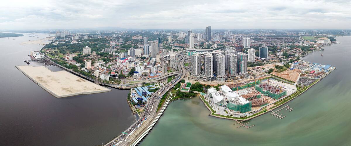 A coastal cityscape with high-rise buildings, a bridge, and a marina.