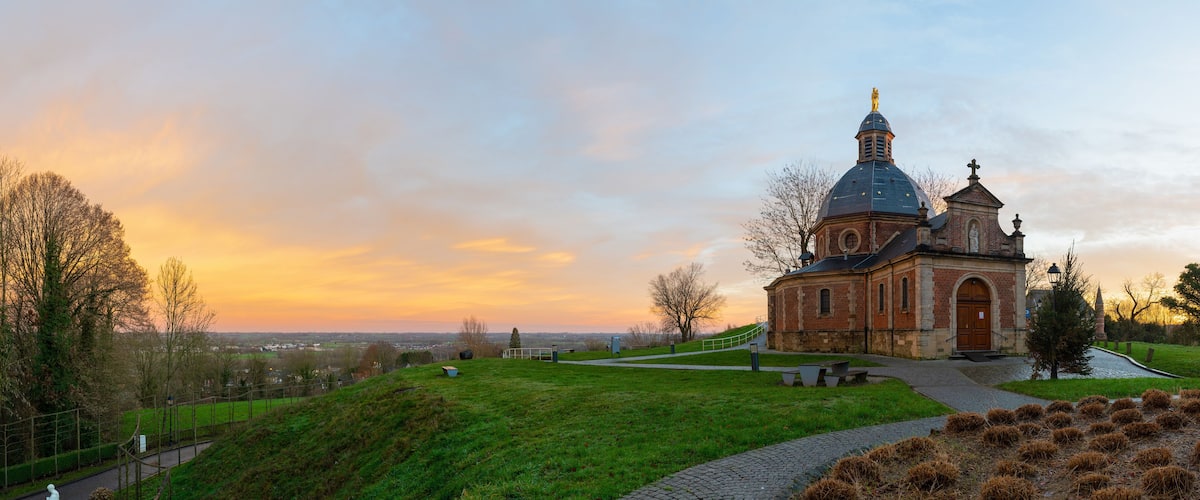 A church with a dome and bell tower, surrounded by a grassy hill and a cobblestone path.