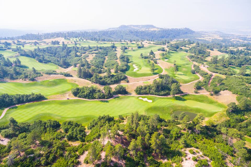 A golf course with multiple greens, sand bunkers, and wooded areas.