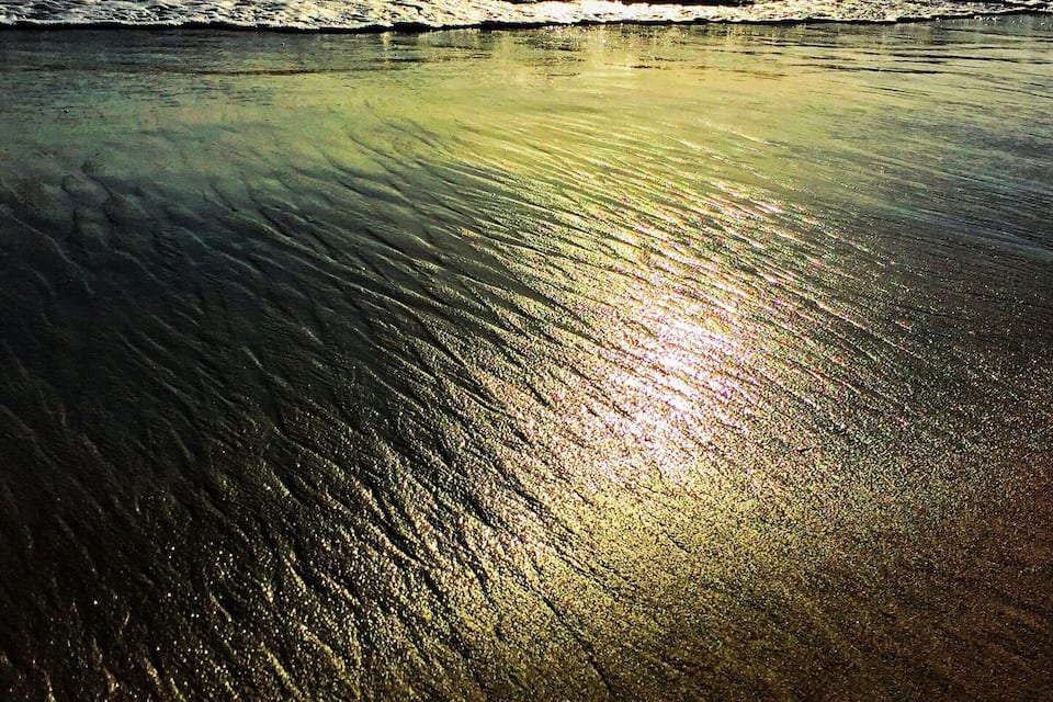 Ein Strand mit Sonnenlicht, das auf feuchtem Sand reflektiert.