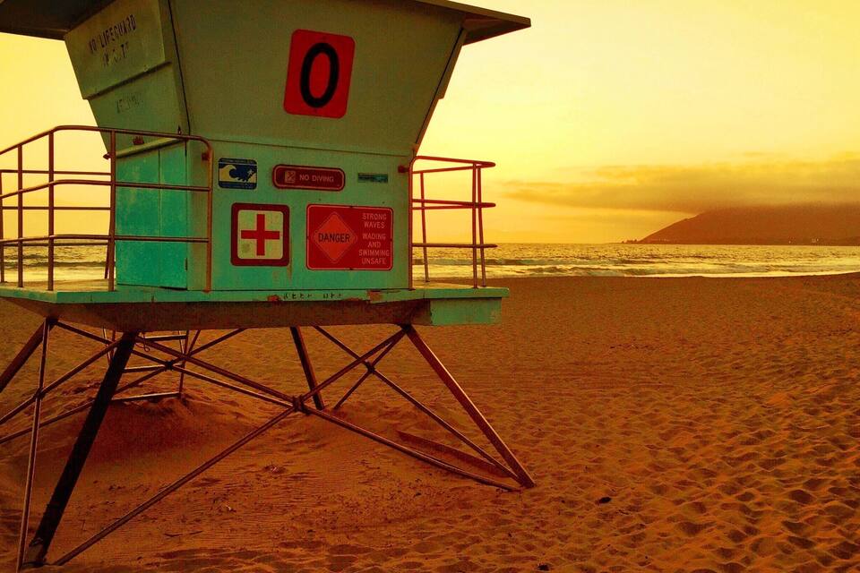 A lifeguard tower on a beach with warning signs.